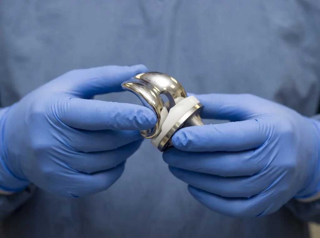Gloved hands holding a metal and plastic knee replacement implant