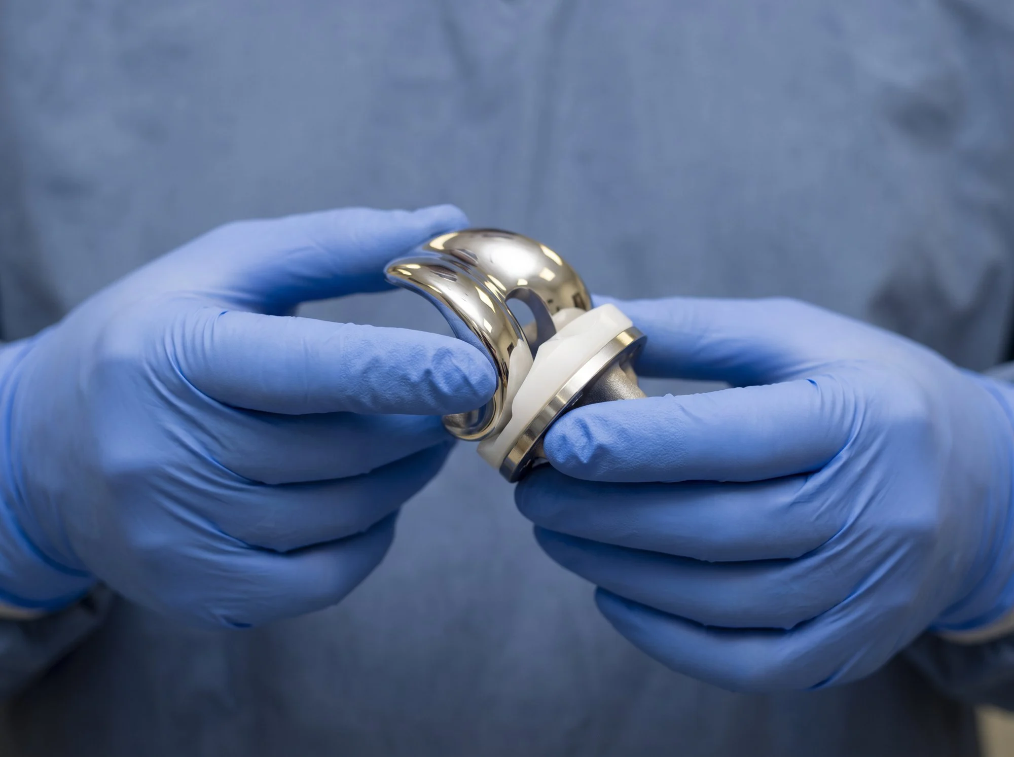 Gloved hands holding a metal and plastic knee replacement implant